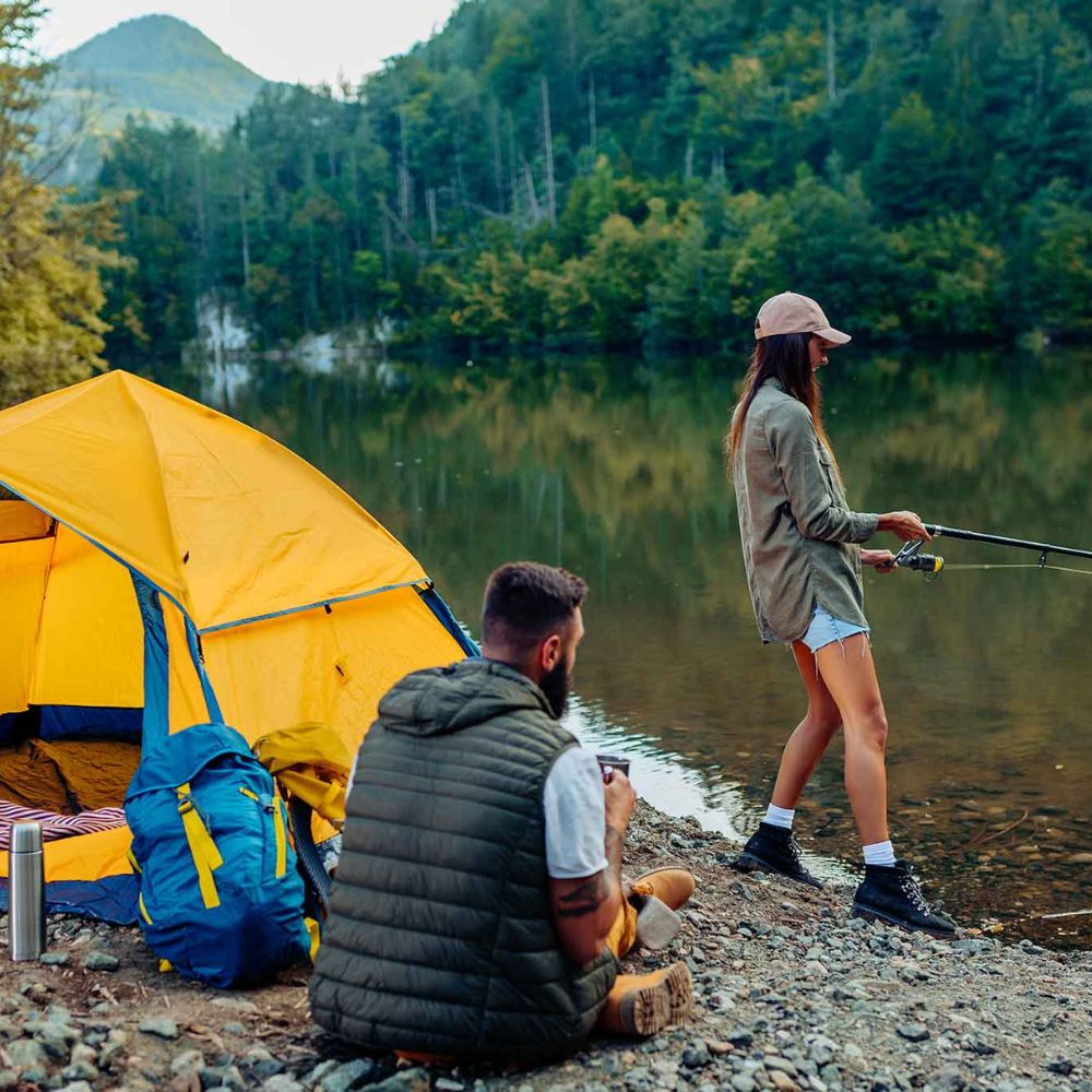Two people by a lake with a yellow tent and fishing rod.

