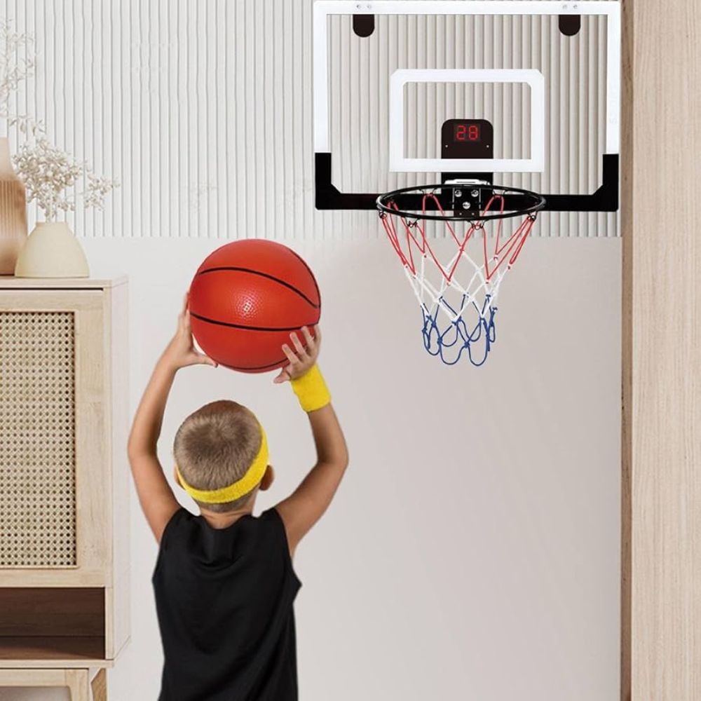 Child holding a basketball in front of a mini basketball hoop on a wall.

